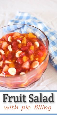 a glass bowl filled with fruit salad on top of a blue and white checkered cloth