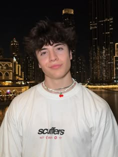 a young man standing in front of a body of water with a city skyline behind him