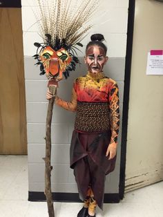 a person in costume standing next to a tree with two masks on it's head