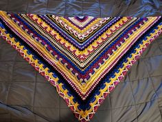 a crocheted triangle is laying on a quilted bed spread with blue, yellow and red colors