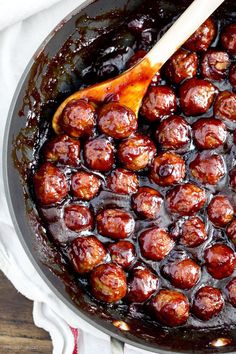 a wooden spoon in a pot filled with cooked meatballs and barbecue sauce on the side