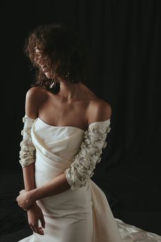 a woman in a white dress with flowers on her arms and shoulder, posing for the camera