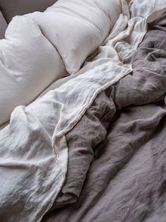 an unmade bed with white and grey linens