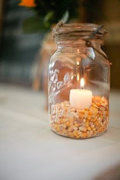 a mason jar filled with corn and a lit candle sitting on top of a table