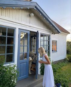 a woman standing in front of a blue door next to a white house with a dog