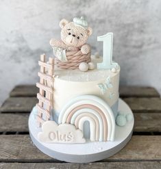 a teddy bear sitting on top of a cake with a rainbow and number one in the middle