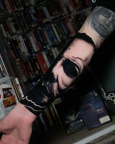 a man's arm covered in tattoos with a skull and sunglasses on it, next to a bookshelf