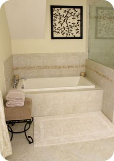 a white bath tub sitting next to a walk in shower and a bench with towels on it