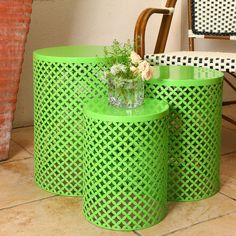 two green side tables with vases and flowers on them in front of a chair