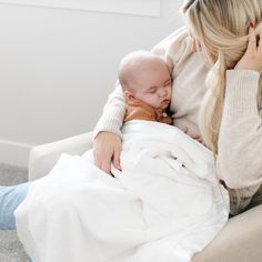 a woman holding a baby wrapped in a blanket while sitting on a couch next to her