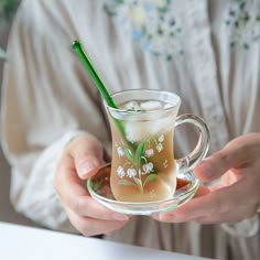 a woman holding a glass cup filled with liquid and a green straw in her hand