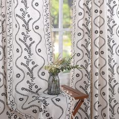 a vase with flowers sitting on top of a table in front of a curtained window