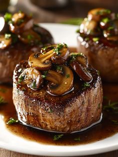 three steaks with mushrooms and sauce on a white plate, ready to be eaten