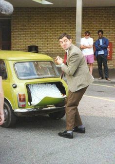 a man standing next to a small green car