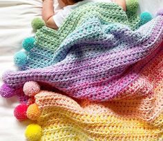 a crocheted blanket with pom - poms on it and a teddy bear laying next to it