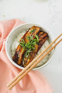 two chopsticks in a bowl with rice and chicken on the side next to some chop sticks