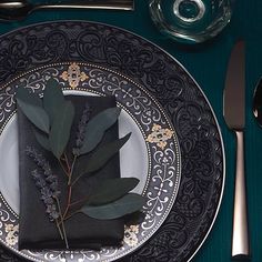 a place setting with silverware, napkins and green leafy leaves on the plate