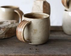 three coffee mugs sitting on top of a wooden table next to rocks and wood slices