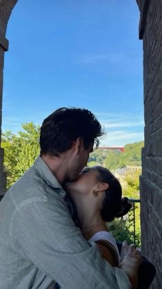 a man and woman kissing each other in an archway between two brick buildings with trees on the other side