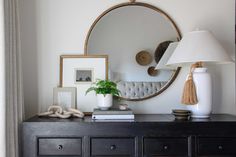 a black dresser topped with a white vase and a mirror