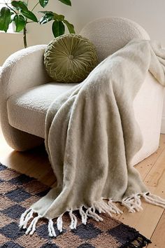 a chair with a blanket on it next to a potted plant and a pillow