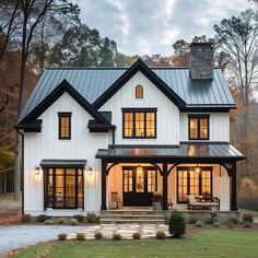 a large white house with black trim and lots of windows on the front porch, surrounded by trees