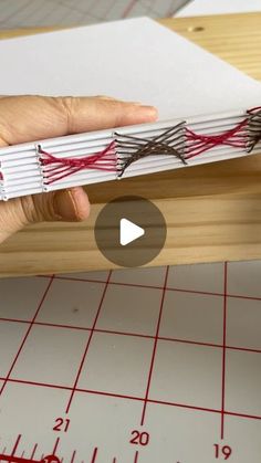 a person is holding an open book with red string on it and measuring the width