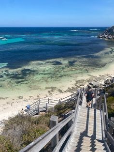 two people walking up stairs to the beach with clear blue water and white sand in the background