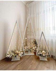 three white christmas trees with ornaments on them in front of a sheer curtained window