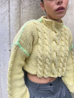 a woman wearing a yellow sweater and grey pants standing in front of a concrete wall