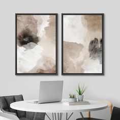 two paintings hanging on the wall above a table with chairs and a laptop in front of it