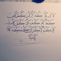 an arabic calligraphy written in blue ink on a piece of paper next to a ball of thread