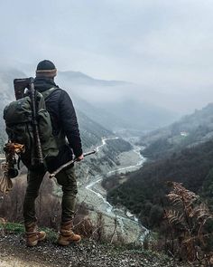 a man with a backpack is standing on a hill looking out at the valley below