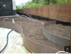 an outdoor garden area with large metal planters filled with dirt and hoses connected to the ground