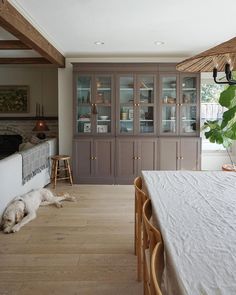 a dog laying on the floor in front of a dining room table and china cabinet