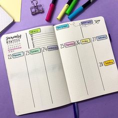 an open planner book sitting on top of a purple table next to markers and pens