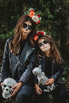 two women with skeleton makeup and flowers on their head sitting next to each other in the woods