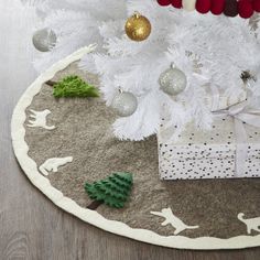 a white christmas tree with presents under it on the floor next to a gift box