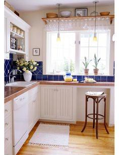 a kitchen with white cabinets and blue tile backsplash, wooden flooring and counter tops