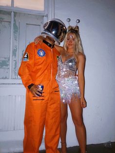 a man in an orange space suit and woman in silver dress standing next to each other