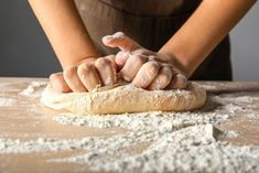 a person kneading dough on top of a wooden table with flour all over it