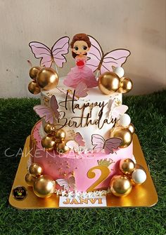 a pink and gold birthday cake sitting in the grass