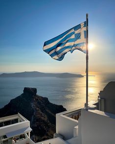 a flag on top of a building with the sun setting over water in the background