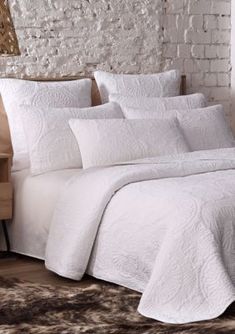 a bed with white sheets and pillows in a room next to a brick wall,