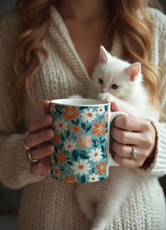 a woman holding a cup with a white cat in it