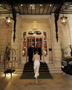 a woman is walking out of the front door of a building with stairs and chandeliers