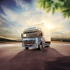 a man standing in front of a truck on the road with trees and sky in the background