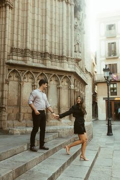 a man and woman holding hands while walking up some steps in front of a building