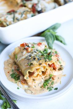 a white plate topped with lasagna covered in sauce and vegetables next to a casserole dish