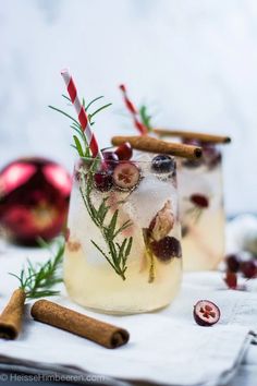 two glasses filled with ice and cinnamons on top of a white cloth next to christmas decorations